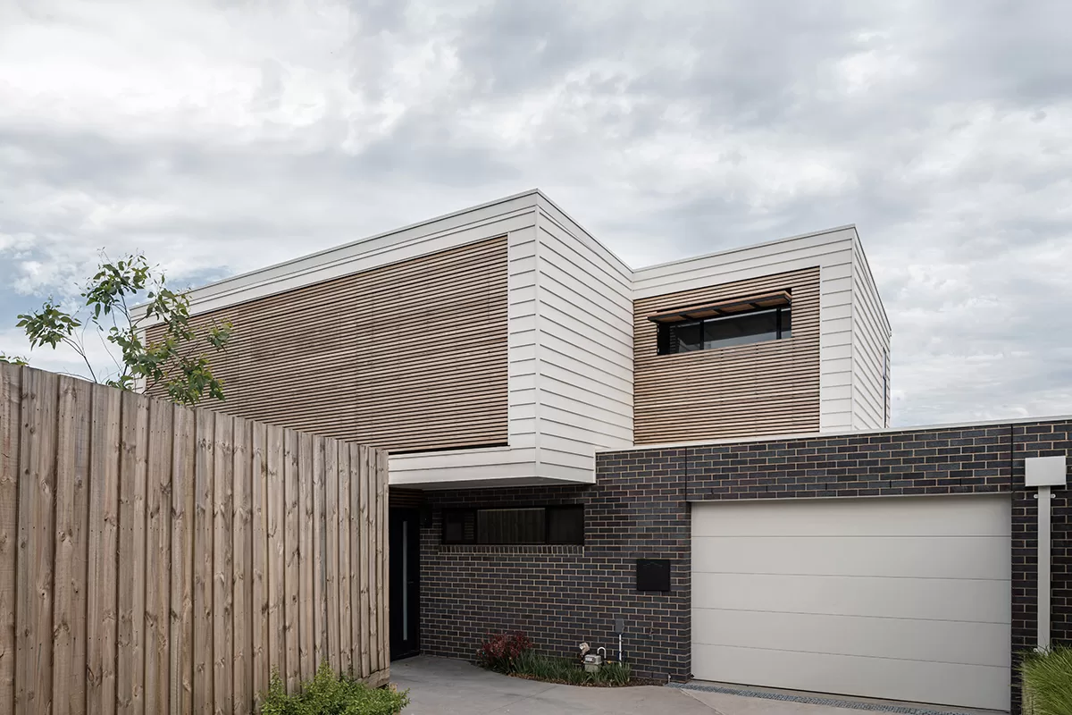 Image of an architect designed new build house.The brick floor is blue-grey brick and the first floor with weatherboard. A timber screen spans the full width of the first floor facade protecting the windows from sun exposure.