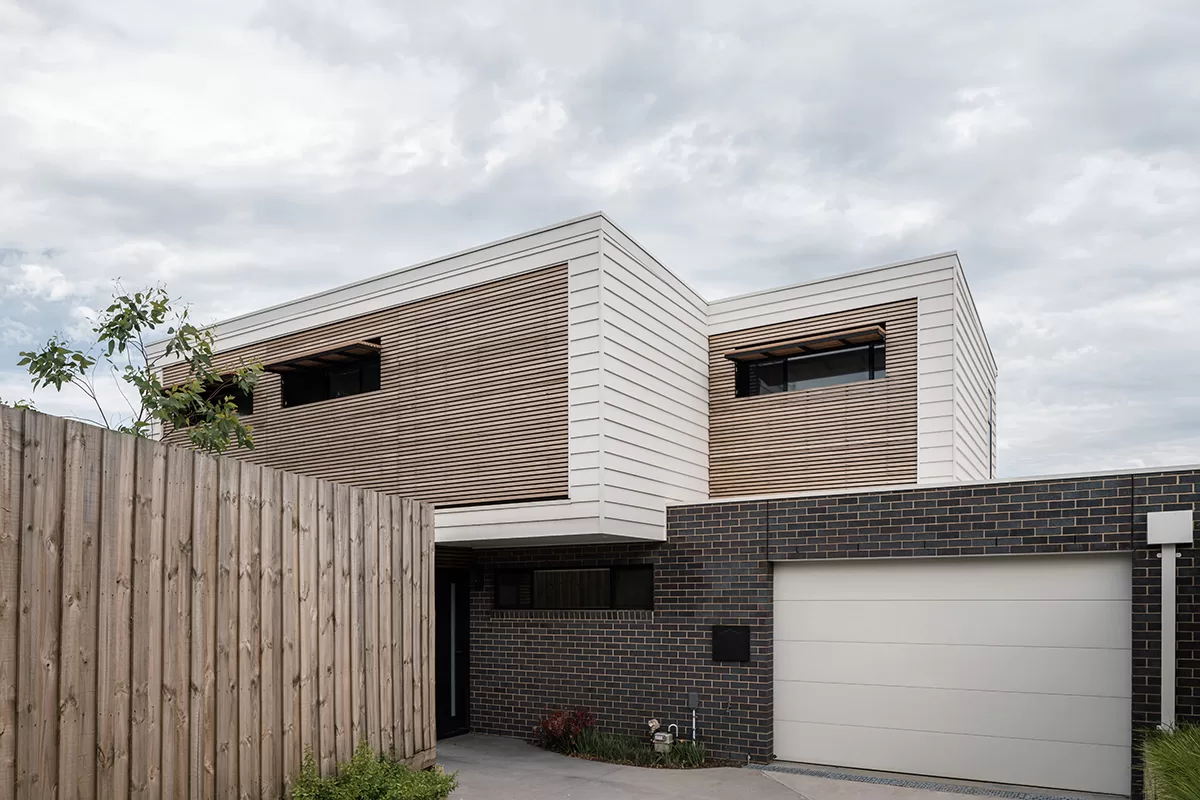 Image of an architect designed new build house.The brick floor is blue-grey brick and the first floor with weatherboard. A timber screen spans the full width of the first floor facade protecting the windows from sun exposure.