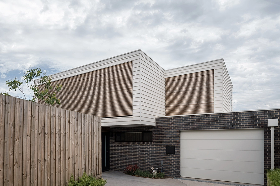 Image of an architect designed new build house.The brick floor is blue-grey brick and the first floor with weatherboard. A timber screen spans the full width of the first floor facade protecting the windows from sun exposure.