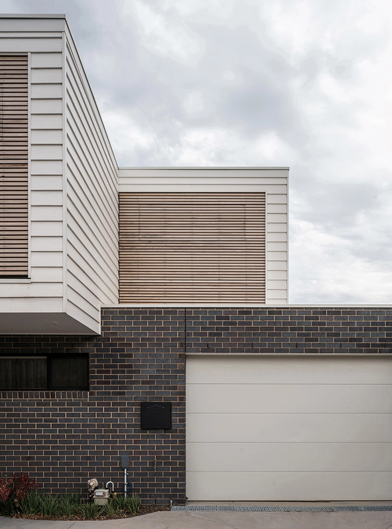 Image of an architect designed new build house.The brick floor is blue-grey brick and the first floor with weatherboard. A timber screen spans the full width of the first floor facade protecting the windows from sun exposure.