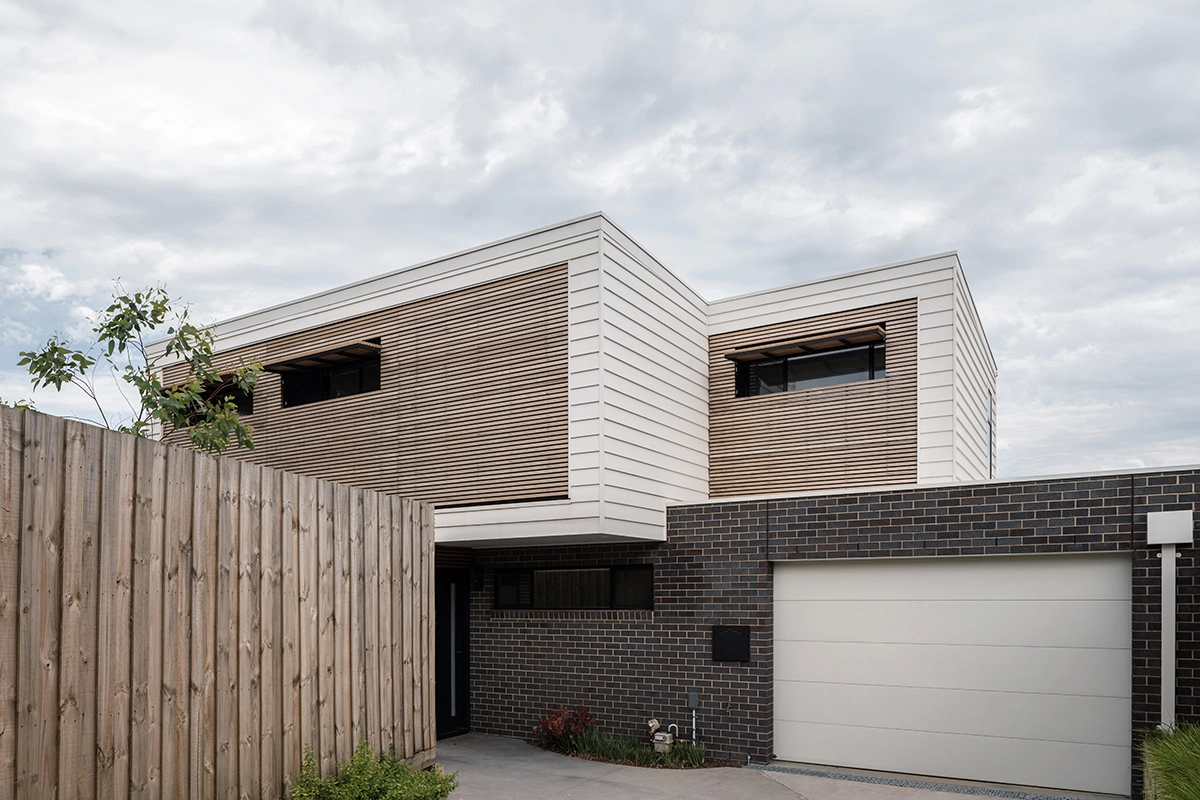 Image of an architect designed new build house.The brick floor is blue-grey brick and the first floor with weatherboard. A timber screen spans the full width of the first floor facade protecting the windows from sun exposure.