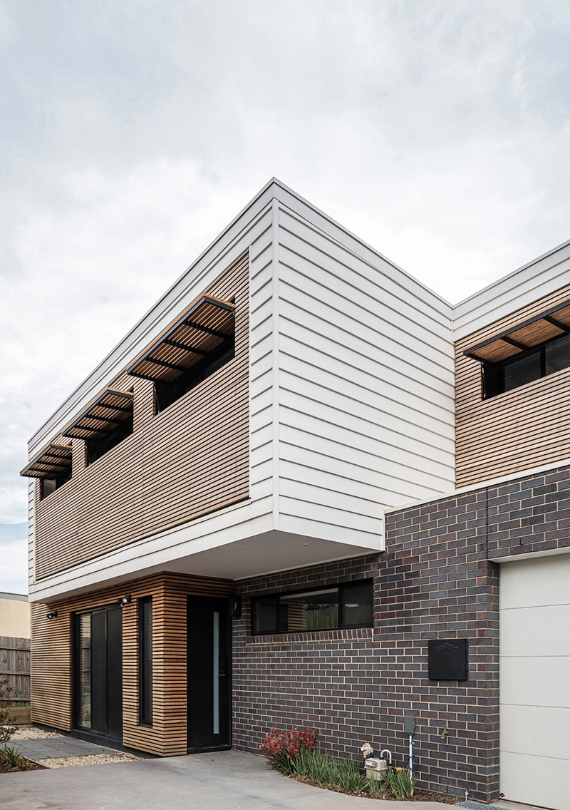 Image of an architect designed new build house.The brick floor is blue-grey brick and the first floor with weatherboard. A timber screen spans the full width of the first floor facade protecting the windows from sun exposure.